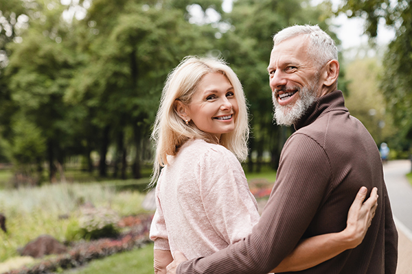 Healthy couple in their late 50s walking through park and holding each other